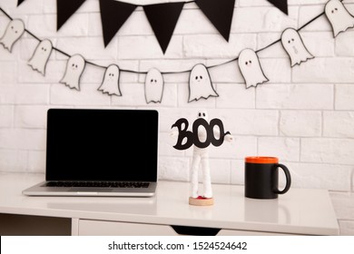 Office Halloween atmosphere. open laptop with blank screen on workplace, holiday ghost figure and black cup - Powered by Shutterstock