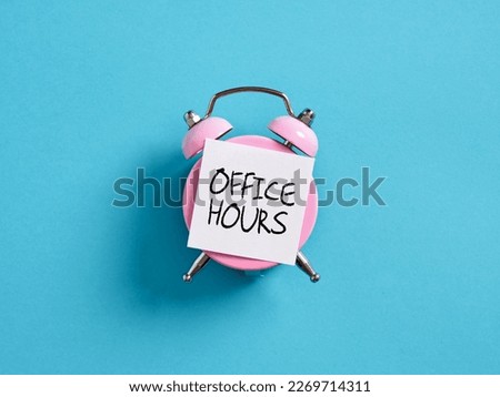 Office hour concept in business or education. Pink alarm clock with a note paper on blue background with the word office hours.