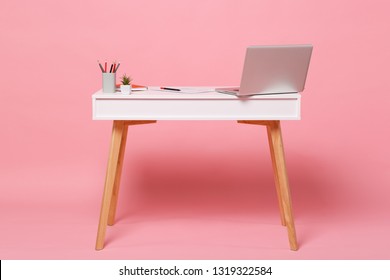 Office light interior of workplace, white table desk with modern laptop pc computer, documents orange notebook pencils, flower isolated on pastel pink wall background in studio. Accessories concept