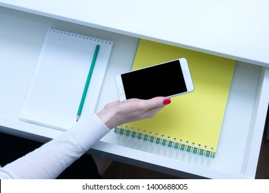 Office Manager holding a white smartphone, female hand, close up, open shelf, white desk, copy space, advertising, top view, 