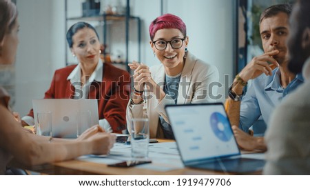 Office Meeting in Conference Room: Beautiful Specialist with Short Pink Hair Talks about Firm Strategy with Diverse Team of Professional Businesspeople. Creative Start-up Team Discusses Big Project