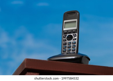 Office Phone Cordless Handset In Docking Station On Table Against Sky Background.