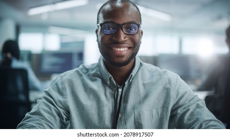 Office: Portrait Of Focused IT Programmer Wearing Headphones Working On Computer, Looking At Camera And Smiling. Black Male Software Engineer Developing Innovative App, Program, Video Game.