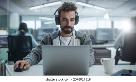 Office: Portrait Of Smiling IT Programmer Wearing Headphones Working On Desktop Computer. Male Website Developer, Software Engineer Developing App, Video Game. Listening To Podcast, Music. Front View