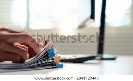 Office professional sorting a stack of paperwork beside a calculator, representing business management and data organization, administrative workload,compliance, deadlines, and business organization.
