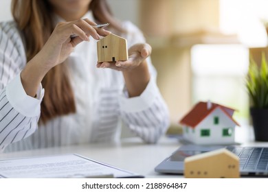 Office Real Estate Agent Holding House Model Working With Calculator And Contract Documents Calculating Home Sale Price.