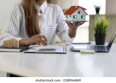 Office Real Estate Agent Holding House Model Working With Calculator And Contract Documents Calculating Home Sale Price.