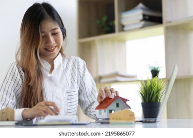 Office Real Estate Agent Holding House Model Working With Calculator And Contract Documents Calculating Home Sale Price.