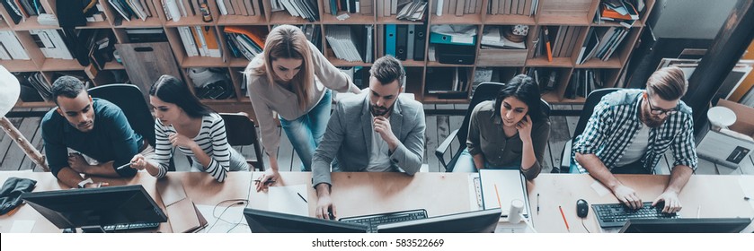 Office Routine. Top View Of Group Of Young Business People In Smart Casual Wear Working Together While Sitting At The Large Office Desk