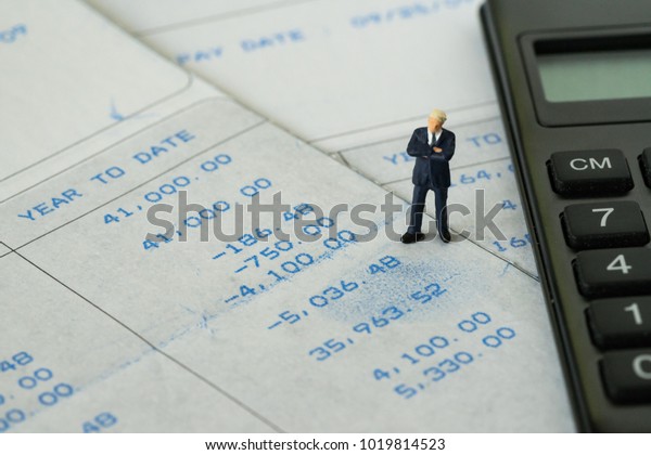 Office\
salary man or tax calculation concept, miniature figure business\
man standing on salary slip with black\
calculator.