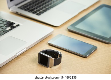 Office setup. Close up of two laptops, tablet and a smartwatch on a wooden office table.