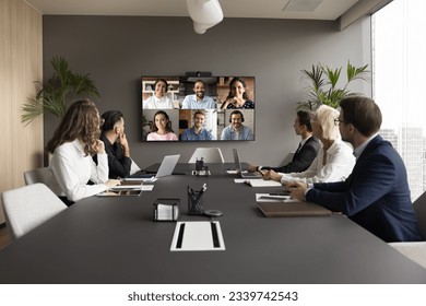 Office staff meeting with diverse freelance team on online video conference, making group call on internet, sitting at table looking at electronic board with head shots, discussing work project - Powered by Shutterstock