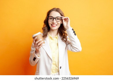 Office Style. business woman in a white suit holds paper cup of coffee and puts on glasses on yellow isolated background, girl manager in jacket with drink smiles - Powered by Shutterstock