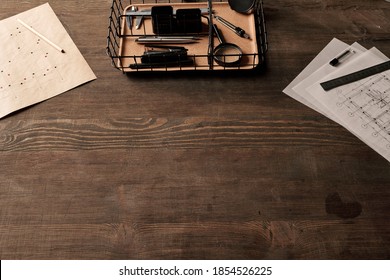 Office supplies and handtools in basket, pencil on blueprint, metallic ruler on papers with sketches surrounding copyspace on wooden table