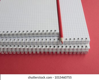 Office supplies: a pile of white notebooks and a red pencil on a red background. Education. Business. The concept. Top view. Copy space. ?lose-up.