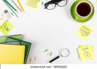 Office Table Desk With Green Supplies, Blank Note Pad, Cup, Pen, Glasses, Crumpled Paper, Magnifying Glass, Flower On White Background. Top View