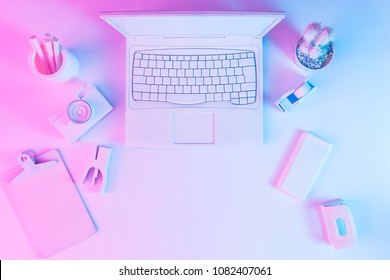 Office Table With Notebook Computer, Camera And Smartphone Painted In White With Vibrant Bold Gradient Purple And Blue Holographic Color Lights. Concept Art. Minimal Office Surrealism.