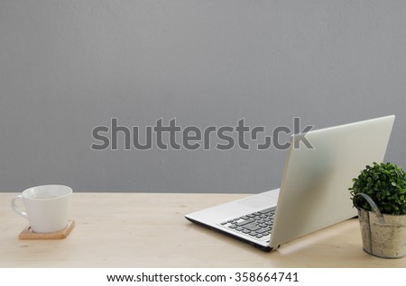 Office table with notebook, green tree on basket  and white coffee cup. View from front with notebook space.