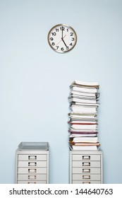 Office wall with clock stack of paperwork in outbox on file cabinet