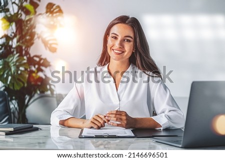 Office woman smiling, looking at the camera with contract on work desk. Smiling manager working in office room. Concept of secretary and reception