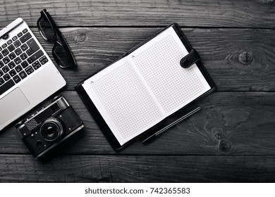 Office work space with camera, notebook, eyepieces, and pen. On a wooden surface. Top view. Free space for your text.
