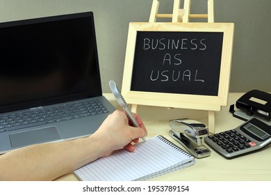 An Office Worker Carrying Out Office Duties And A Chalkboard With The Words Business As Usual. - Shutterstock ID 1953789154