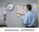 Office worker checking notes on pin board and holding documents.