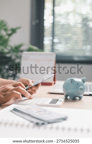 Office worker counting cash while using a calculator beside a piggy bank, illustrating personal finance, saving money, budgeting, expense tracking and financial management in modern workspace.