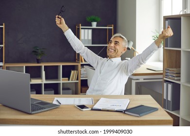 Office Worker Feeling Happy After Finishing Project And Enjoying Satisfaction With A Job Well Done. Senior Business Man Sitting At Desk With Laptop, Smiling And Leaning Back With Arms Outstretched