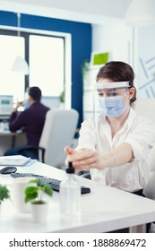 Office Worker Following Safety Precaution During Global Pandemic With Coronavirus Applying Sanitizer. Businesswoman In New Normal Workplace Disinfecting While Colleagues Working In Background.