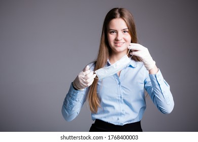 Office Worker Girl Removes A Medical Mask And Smiles Lifting Quarantine On A Gray Background.