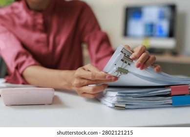 Office worker hands sorting and compiling stacks of white paper documents, secured with colorful binder clips, creating an organized system for administrative tasks and reporting