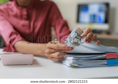 Office worker hands sorting and compiling stacks of white paper documents, secured with colorful binder clips, creating an organized system for administrative tasks and reporting