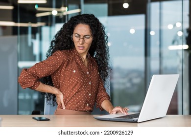 Office Worker Latin American Business Reaper Is Sick At The Workplace, An Overtired Businesswoman Has Back Pain, Massages Her Back With Her Hand.