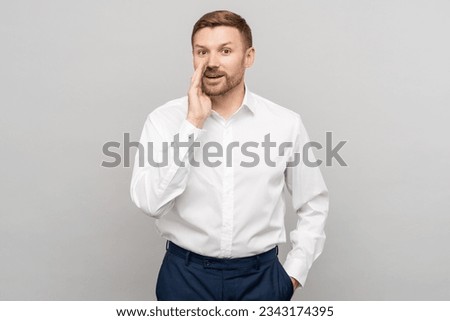 Office worker man whispering with hand near mouth gesture on grey studio background. Advertisement banner. Smiling positive businessman shares a secret offer, looking at camera talking secret. 