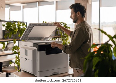Office worker operating a multifunction printer, making photocopies and scanning important documents in a modern office environment filled with greenery and natural light. Technology concept