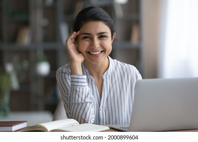 Office worker. Positive young mixed race woman employee manager pose for portrait by work desk with pc paper notebook. Teenage indian female student look at camera with smile distracted from paperwork