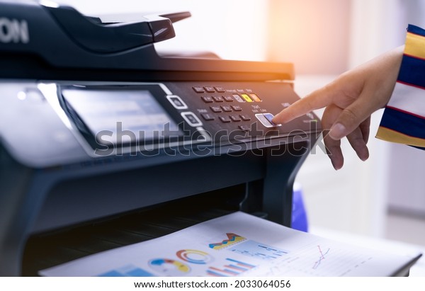 Office worker print paper on multifunction laser\
printer. Copy, print, scan, and fax machine in office. Modern print\
technology.  Photocopy machine. Document and paper work.\
Professional scanner.
