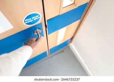 Office worker seen about to open a fire door located within a government owned building. The door will automatically shut to prevent ingress of a fire.