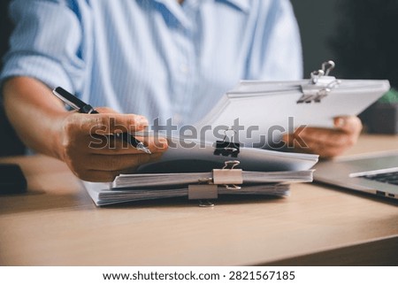 Office worker sorting and reviewing clipped document stacks beside a laptop, representing paperwork organization, file management, administrative processes, record keeping,