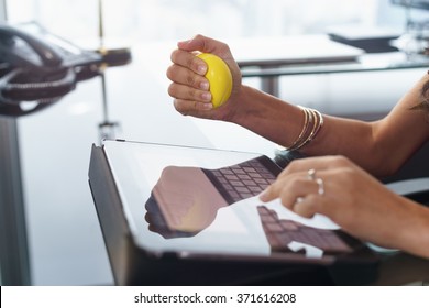 Office Worker Typing Email On Tablet Computer. The Woman Feels Stressed And Nervous, Holds An Antistress Yellow Ball In Her Hand