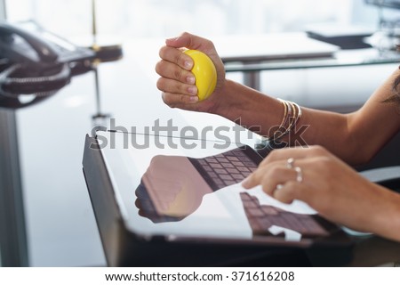 Office worker typing email on tablet computer. The woman feels stressed and nervous, holds an antistress yellow ball in her hand