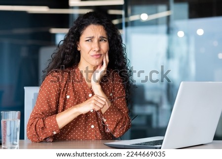 Office worker at work inside the office has a bad toothache, Latin American business woman at work using a laptop.