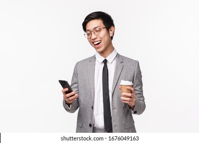 Office workers, business and lifestyle concept. Waist-up portrait of lucky cheerful asian male entrepreneur calling friend using wireless earphones, hold smartphone and take-away coffee, smiling - Powered by Shutterstock