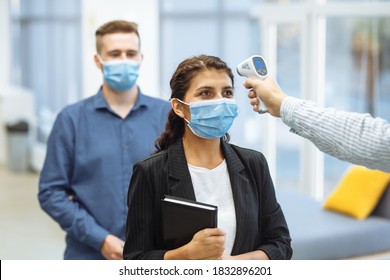 Office workers are checked with a distant non contact thermometer during coronavirus pandemic. Young business woman passing temperature control at the office corridor to prevent covid-19 spread. - Powered by Shutterstock