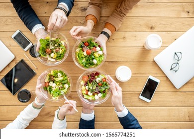 Office workers during a business lunch with healthy salads and coffee cups, view from above on the wooden table