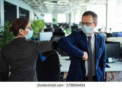 Office Workers Shake Hands When Meeting And Greet Bumping Elbows. A New Way To Greet The Obstructing Spread Of Coronavirus. Man And Woman In Protective Masks Maintain A Social Distance At Work.