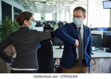 Office workers shake hands when meeting and greet bumping elbows. A new way to greet the obstructing spread of coronavirus. Man and woman in protective masks maintain a social distance at work. - Powered by Shutterstock