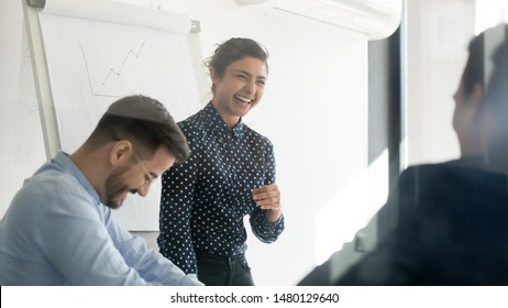 Office Workers Take Break Having Fun Joking Laughing At Business Briefing Lead By Indian Businesswoman In Boardroom View Through Glass Door. Clients And Ceo Meeting Or Team Building Activities Concept