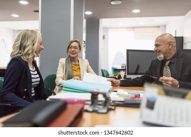 Office Workes Talking And Looking Files: Women And Mature Boss At Desk. Real Enviroment